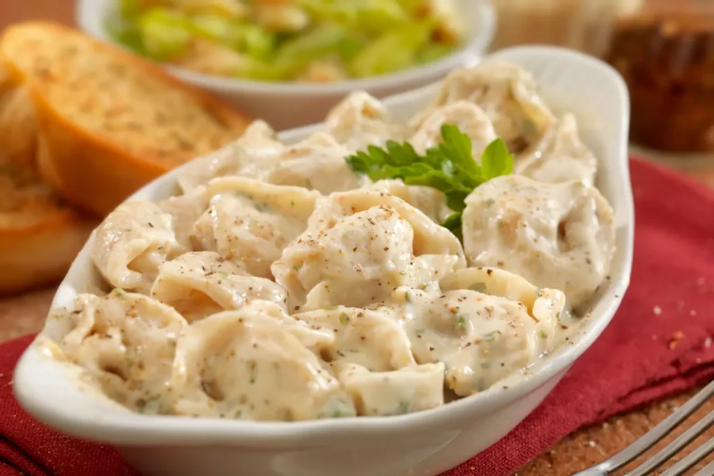 Creamy Chicken Tortellini Alfredo in a white serving bowl Ingredients for Chicken Tortellini Alfredo recipe on kitchen counter